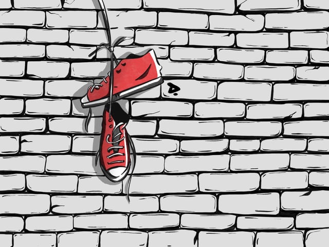 Pair of red high-top sneakers hanging in front of a brick wall.