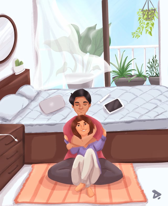Couple sitting together on a sunlit bedroom rug in front of a bed and window.